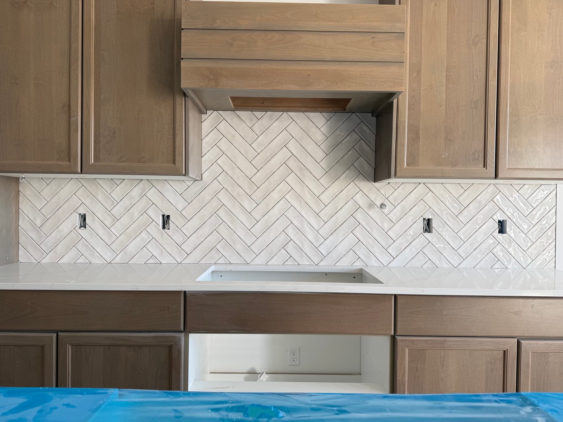 Kitchen with herringbone marble tile backsplash and wood range hood